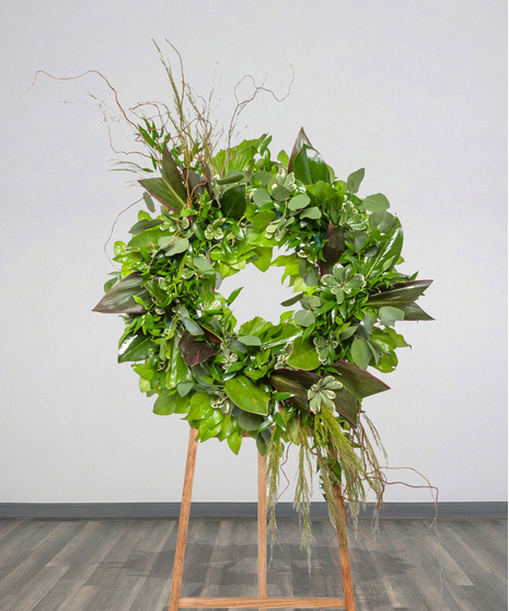 Green funeral wreath with lush foliage and curly willow on a wooden easel from Billy Heroman’s Florist in Baton Rouge