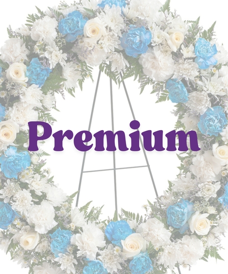 Sympathy wreath of white carnations, blue carnations, and ivory roses displayed on a metal easel – Touch of Color Collection by Billy Heroman’s