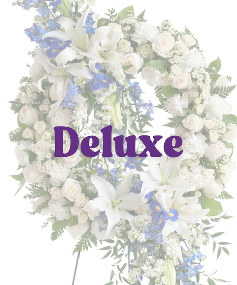 Elegant sympathy wreath with cascading white lilies, blue delphinium, ivory roses, and greenery on a metal easel – Touch of Color Collection by Billy Heroman’s