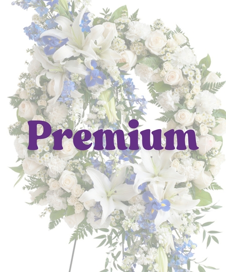 Elegant sympathy wreath with cascading white lilies, blue delphinium, ivory roses, and greenery on a metal easel – Touch of Color Collection by Billy Heroman’s