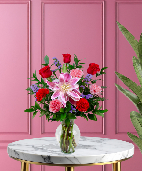 X’s & O’s Valentine's flower arrangement with red roses, pink Stargazer lilies, red and pink carnations, and purple statice in a clear glass vase.