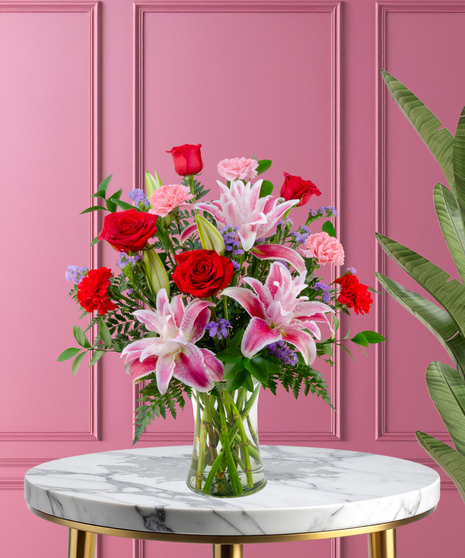 X’s & O’s Valentine's flower arrangement with red roses, pink Stargazer lilies, red and pink carnations, and purple statice in a clear glass vase.