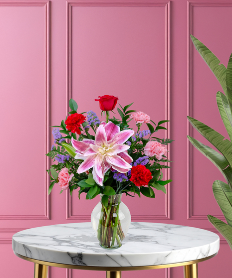 X’s & O’s Valentine's flower arrangement with red roses, pink Stargazer lilies, red and pink carnations, and purple statice in a clear glass vase.