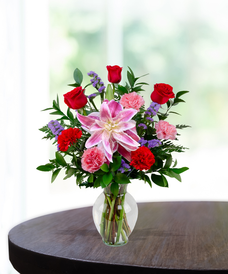 X’s & O’s floral arrangement with red roses, rose lilies, pink carnations, and statice in a clear vase – everyday romantic bouquet.
