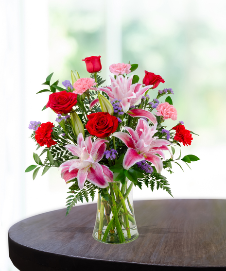 X’s & O’s floral arrangement with red roses, rose lilies, pink carnations, and statice in a clear vase – everyday romantic bouquet.