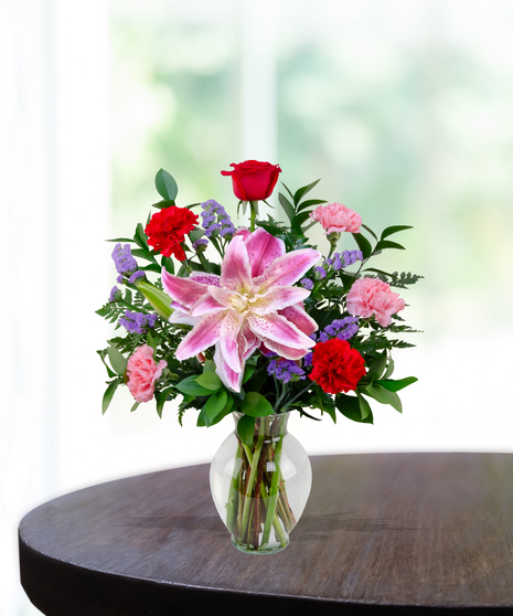 X’s & O’s floral arrangement with red roses, rose lilies, pink carnations, and statice in a clear vase – everyday romantic bouquet.