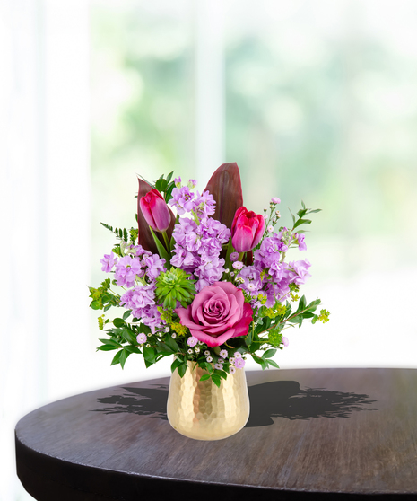 A stunning everyday flower arrangement featuring magenta roses, pink tulips, lavender stock, and a cymbidium orchid in a gold pedestal vase.
