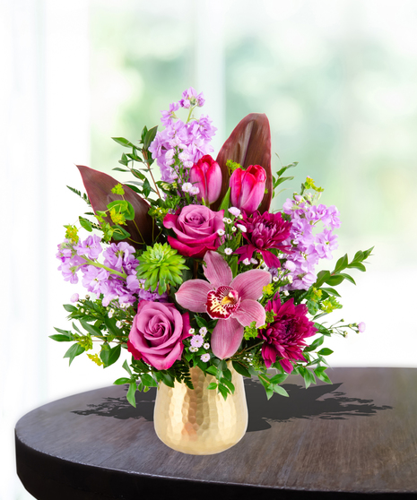 A stunning everyday flower arrangement featuring magenta roses, pink tulips, lavender stock, and a cymbidium orchid in a gold pedestal vase.
